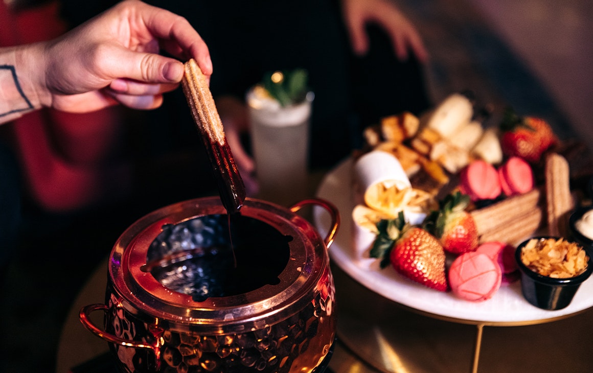 a person dipping a churro into a pot of chocolate